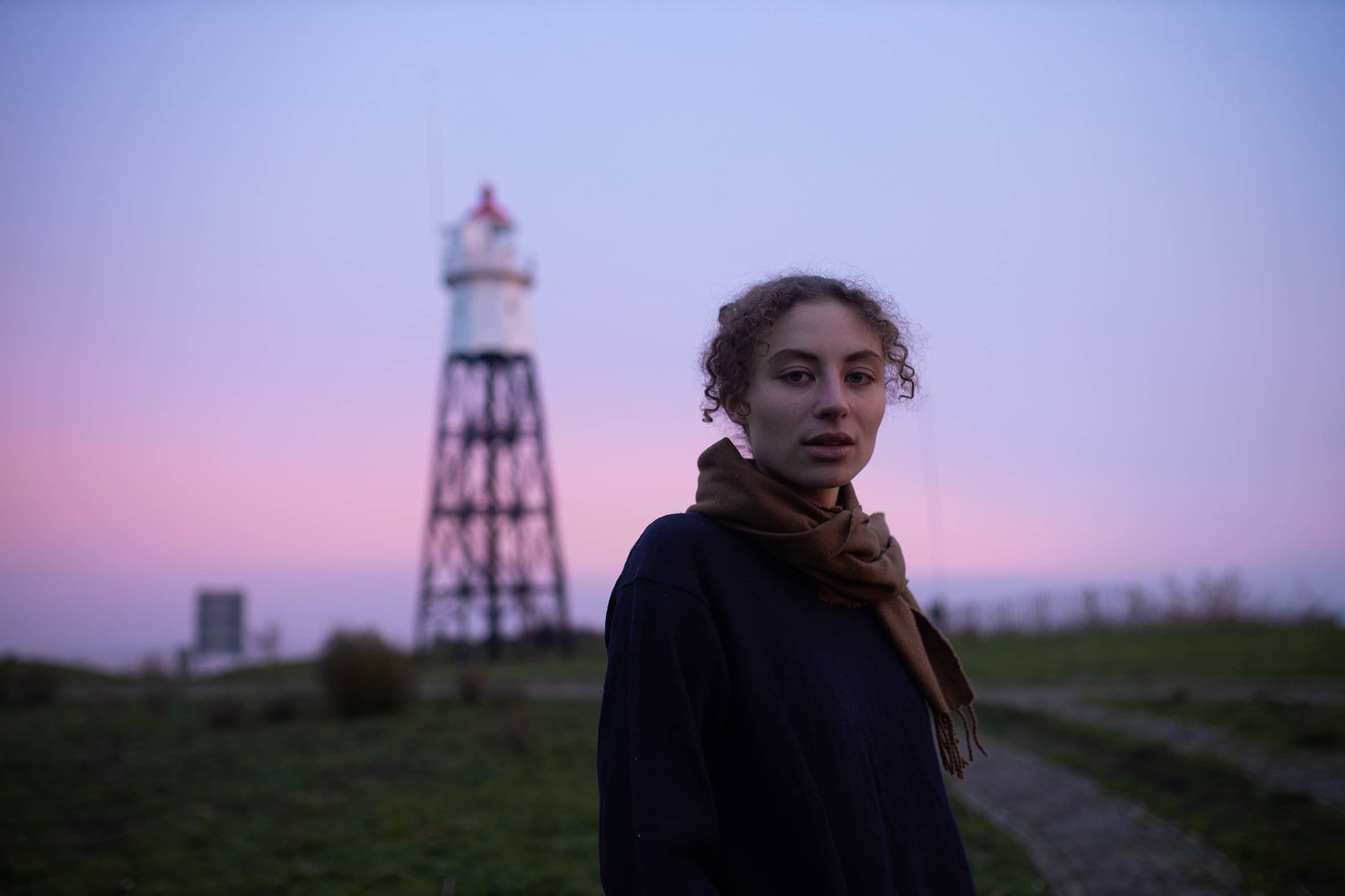 Sarah Neutkens staat bij een spoor tegen een paarse lucht aan en kijkt de camera in.