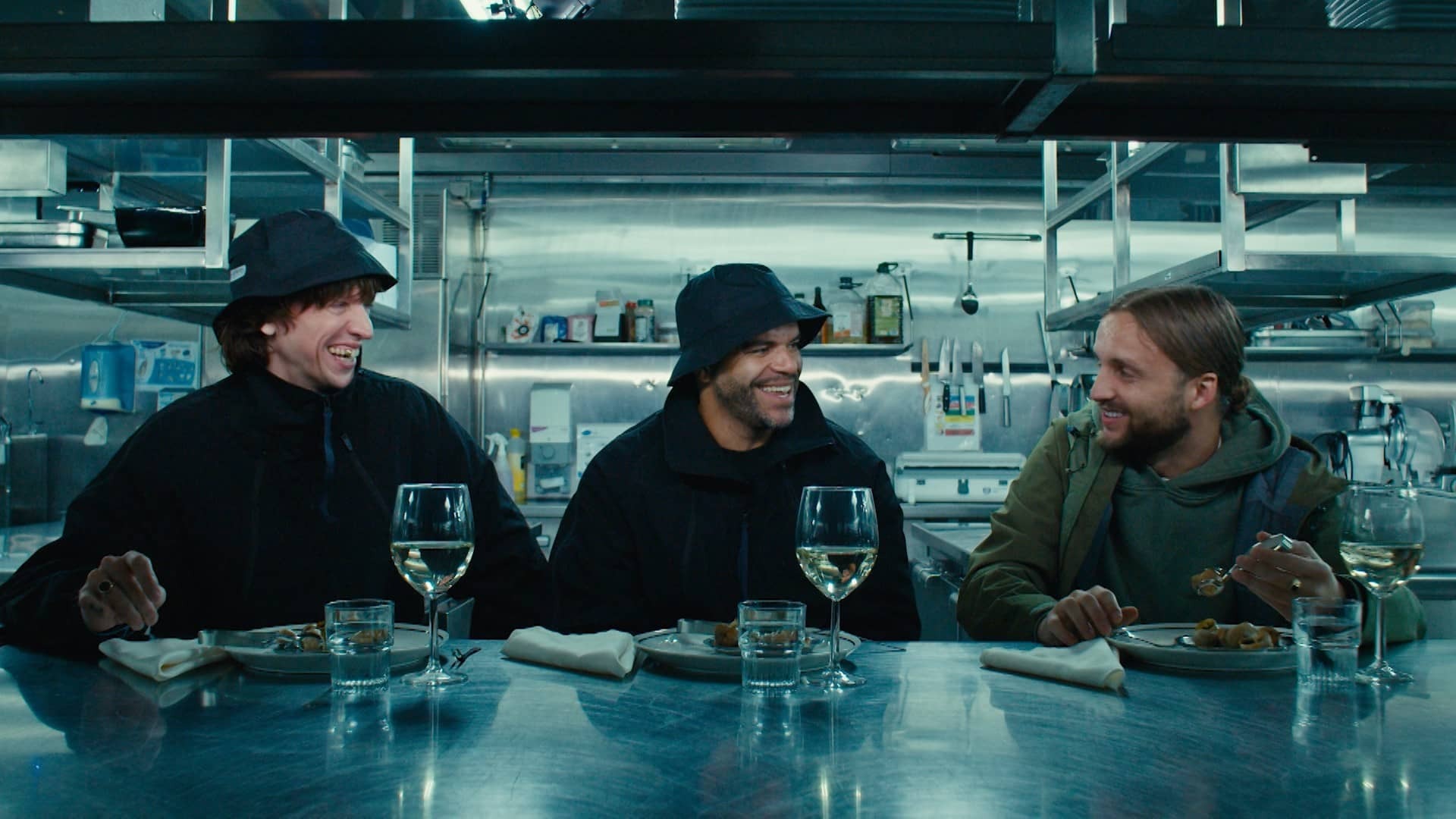 Drie personages uit de serie zitten met elkaar aan tafel.