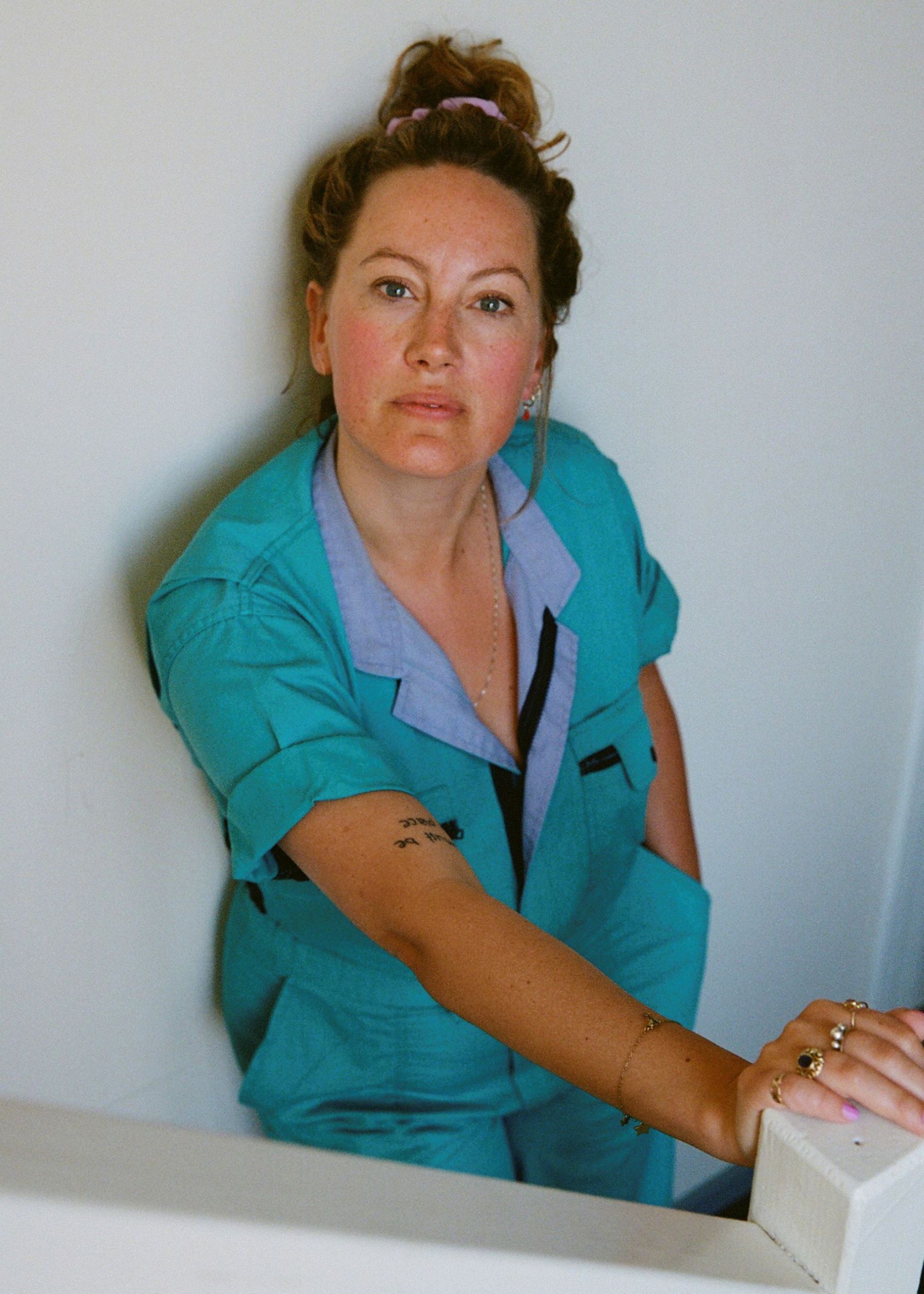 Actrice Laurien van Rijswijk staat tegen een witte muur. Ze draagt een blauwe overal en haar haar in een knot.