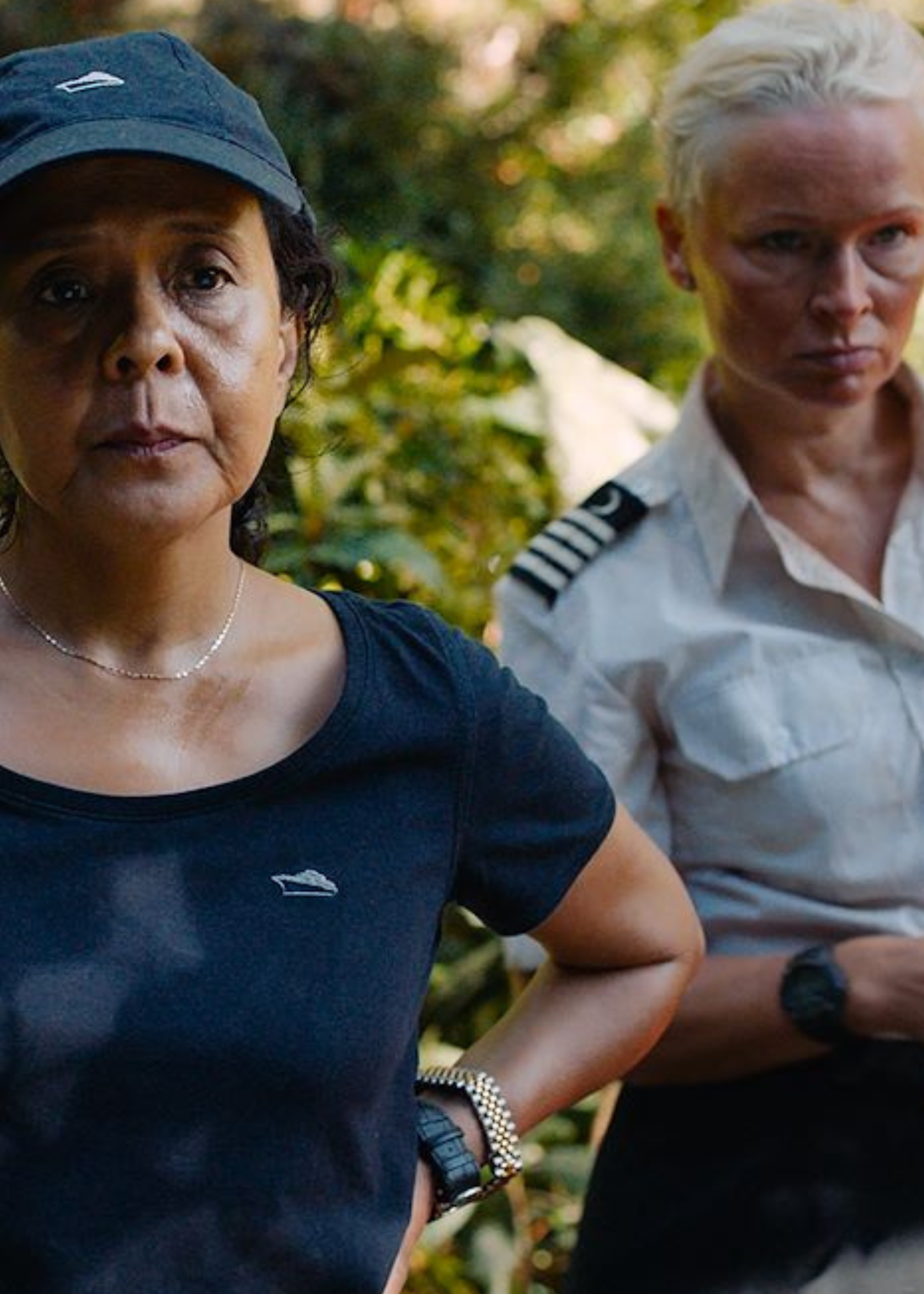 Er staan twee vrouwen op het beeld. De linker vrouw staat met haar handen in haar zij en heeft een zwart T-shirt aan en een zwarte pet op. De rechtervrouw heeft kort geblondeerd haar en heeft een kapiteinkostuum aan.