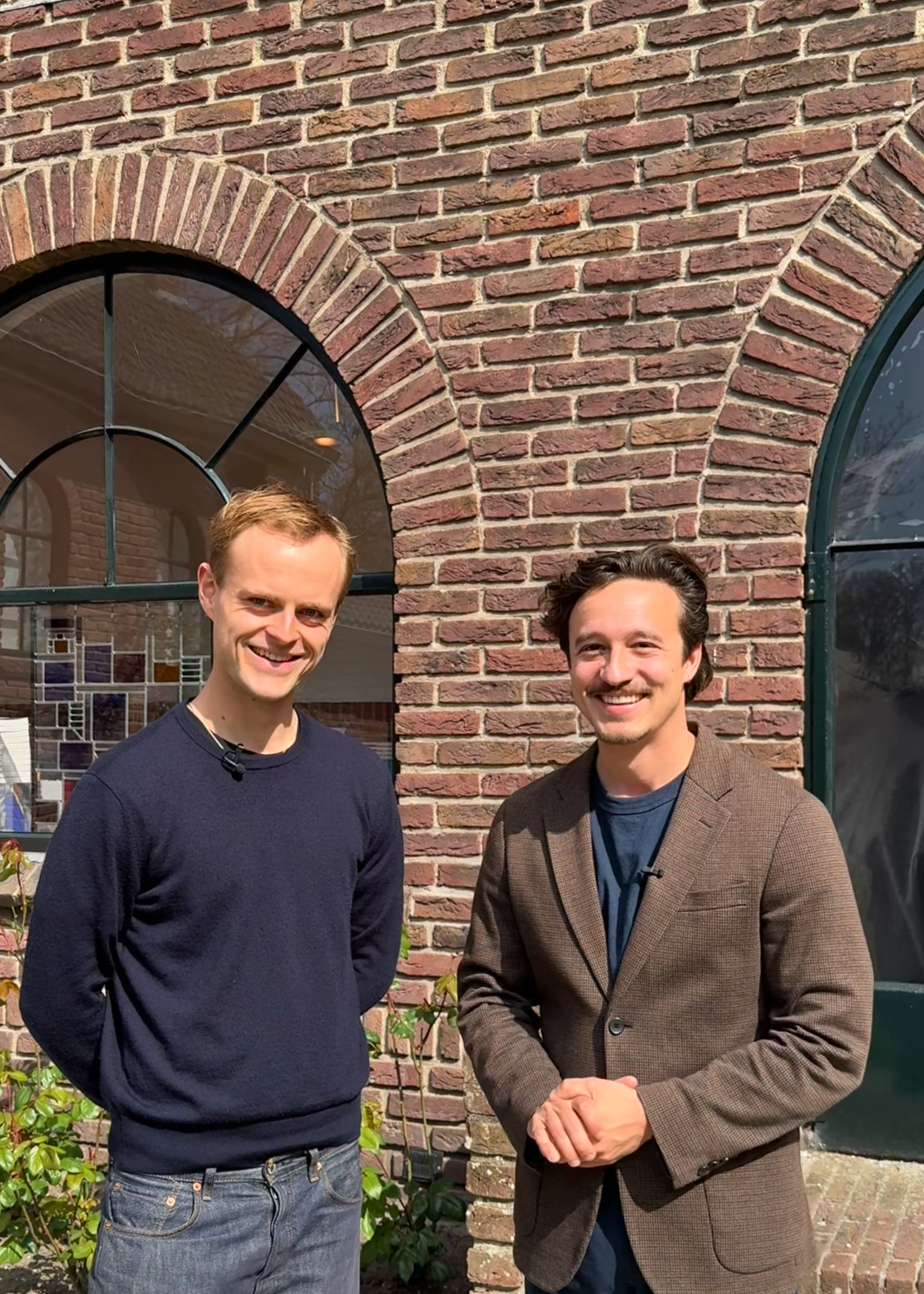 Foto van de twee hoofdrolspelers, Coen en Jurriaan. Ze staan voor een stenenmuur en kijken allebei vriendelijk de camera in.