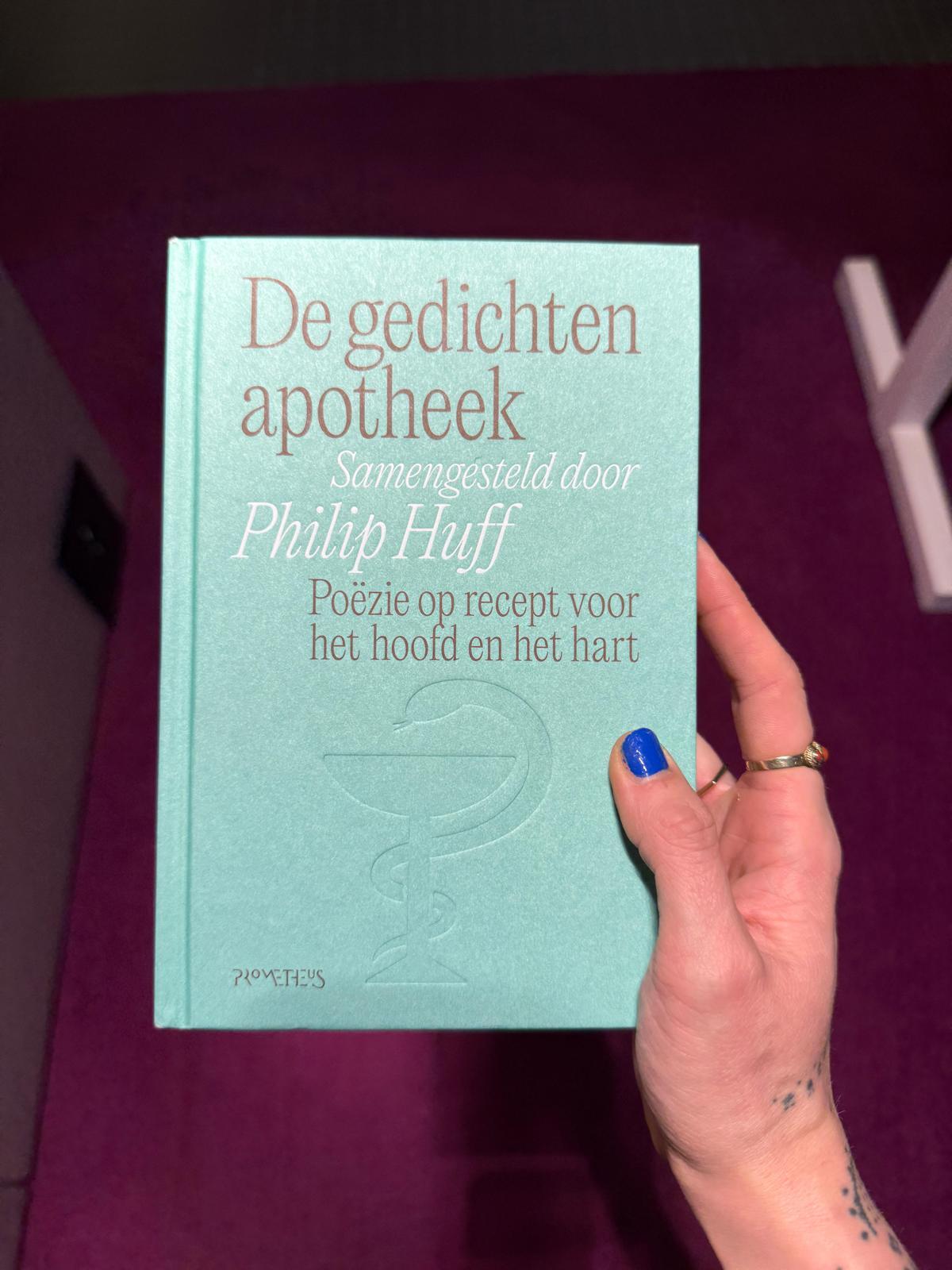Dit is de cover van de gedichtenapotheek. Het boek is turquoise en heeft een watermerk van een apothekerslogo erop staan.
