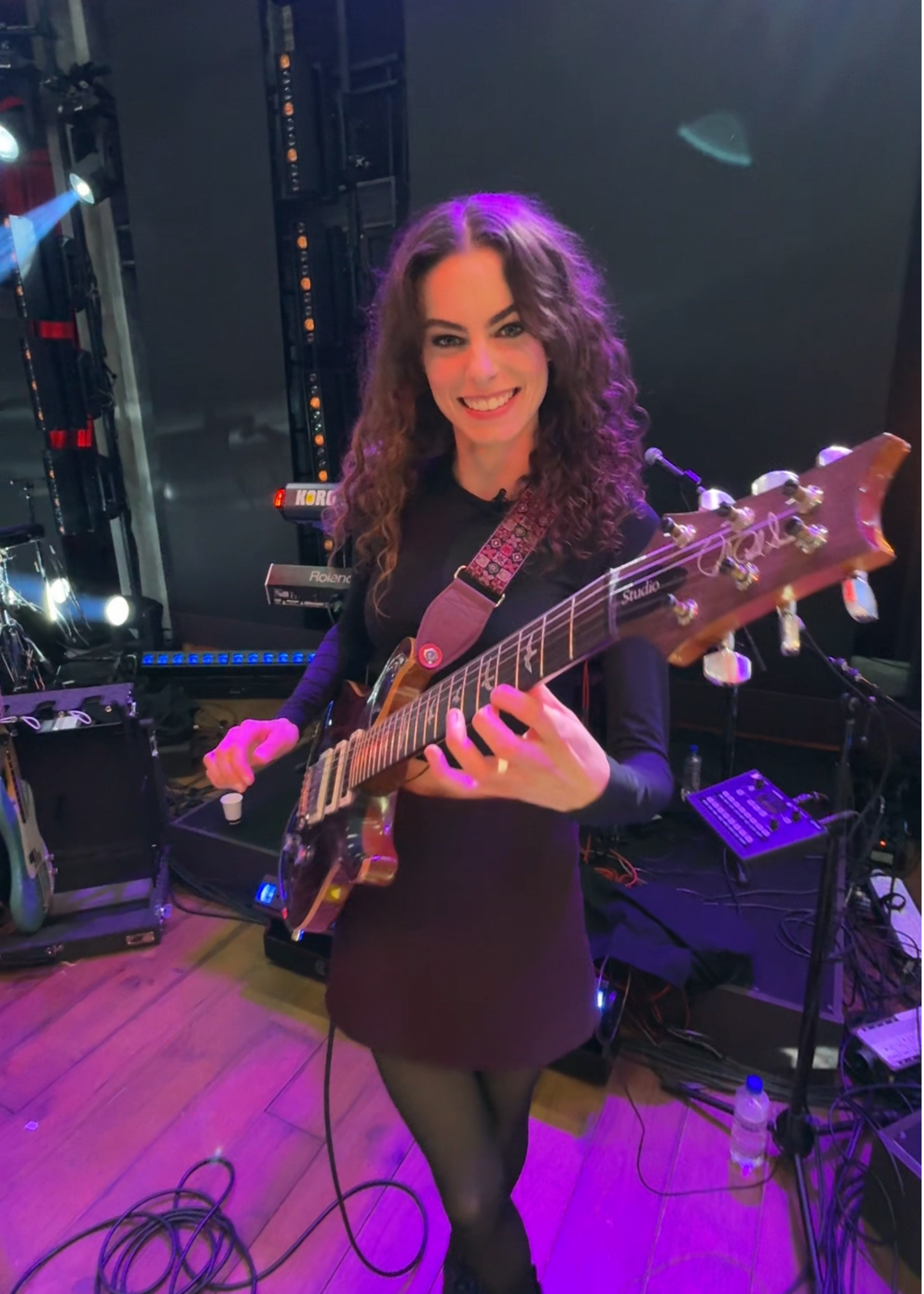 We zien Yvette met haar gitaar in haar handen. Ze staat in een tv studio en kijkt de camera in en lacht. Ze speelt op haar gitaar.