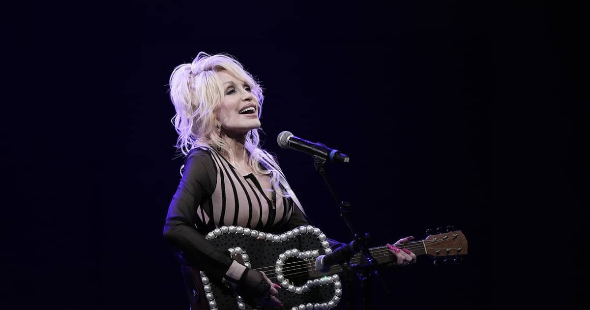 Dolly Parton staat zingend op een podium met een gitaar waarvan de rand is versierd met grote parels.