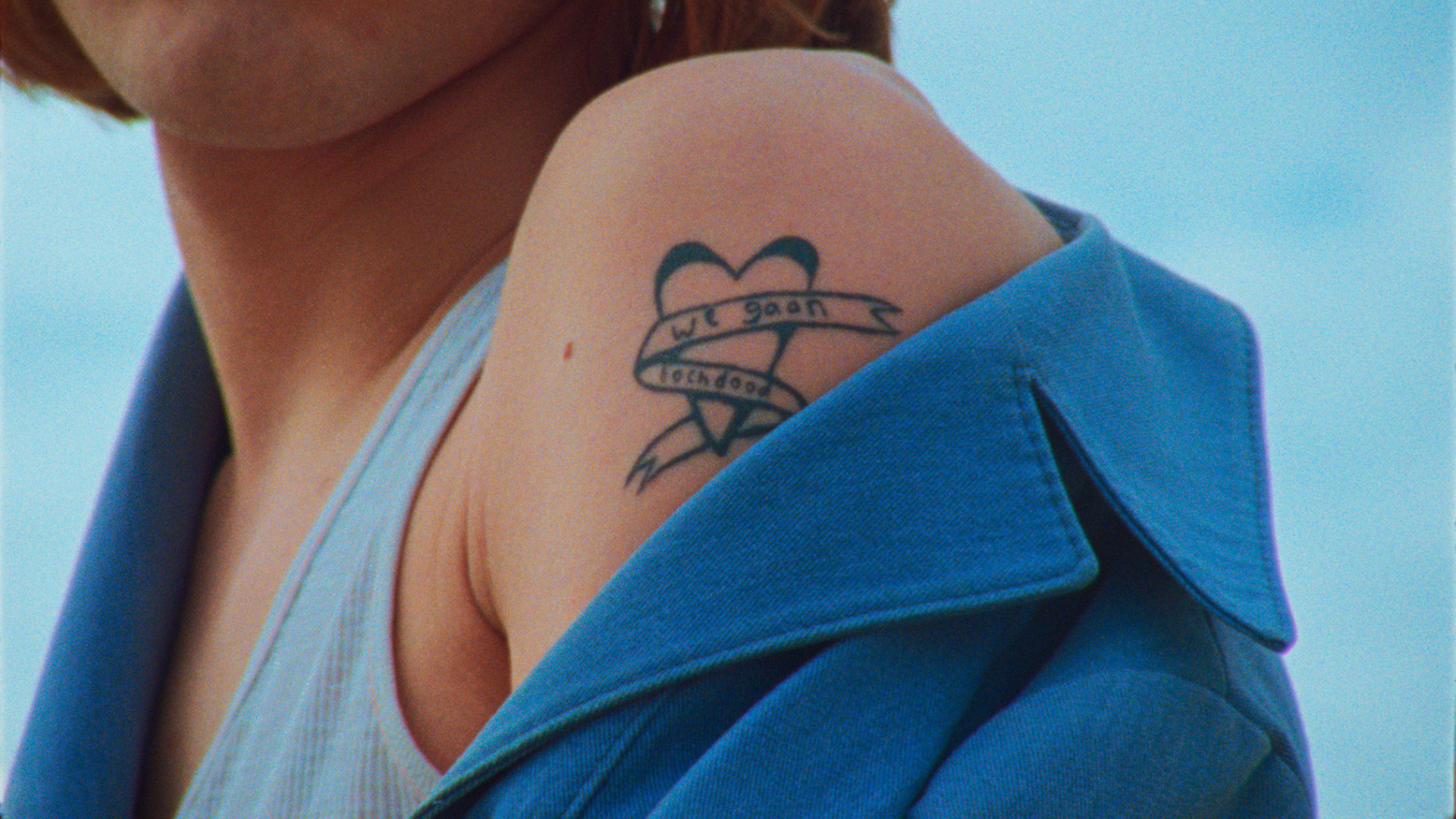 Blote schouder met tattoo. De tattoo is een hart met een lint eromheen, waarop staat 'We gaan toch dood'.