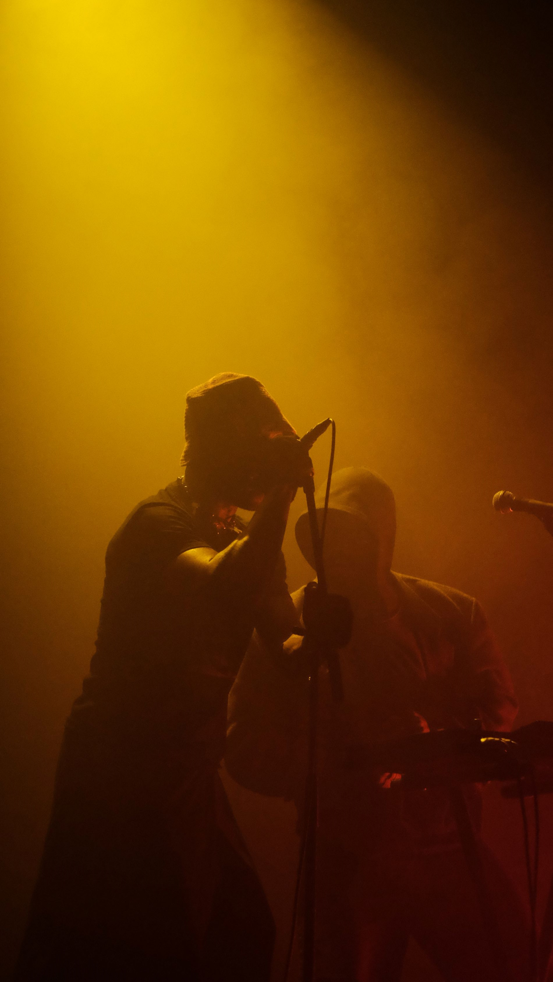 Artiest Isaï staat op het podium op te treden, achter hem staat een man. Het decor bestaat uit gele lampen en veel rook. Beide gezichten van de mannen zijn niet zichtbaar door hoofddeksels.