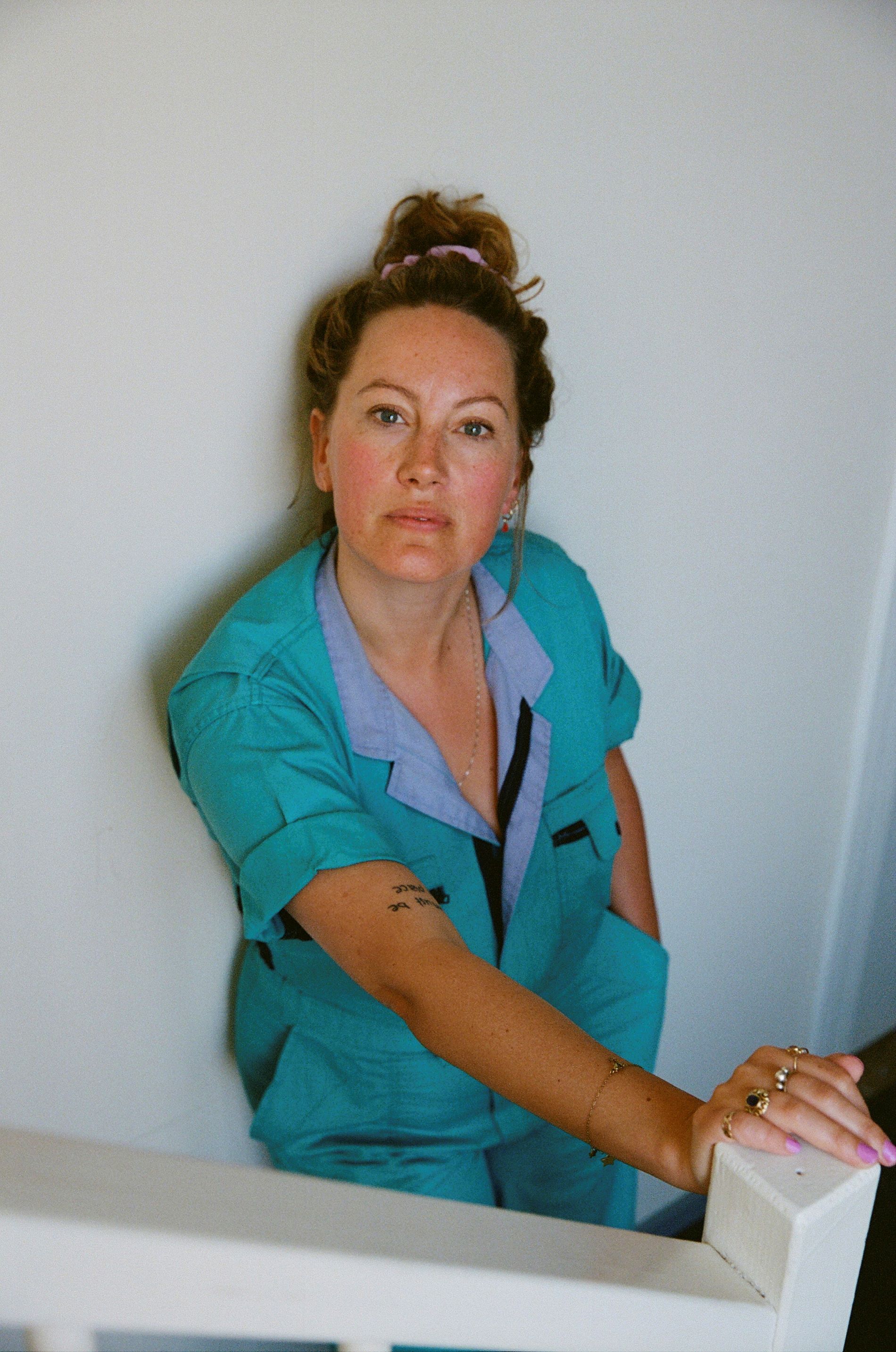 Actrice Laurien van Rijswijk staat tegen een witte muur. Ze draagt een blauwe overal en haar haar in een knot.