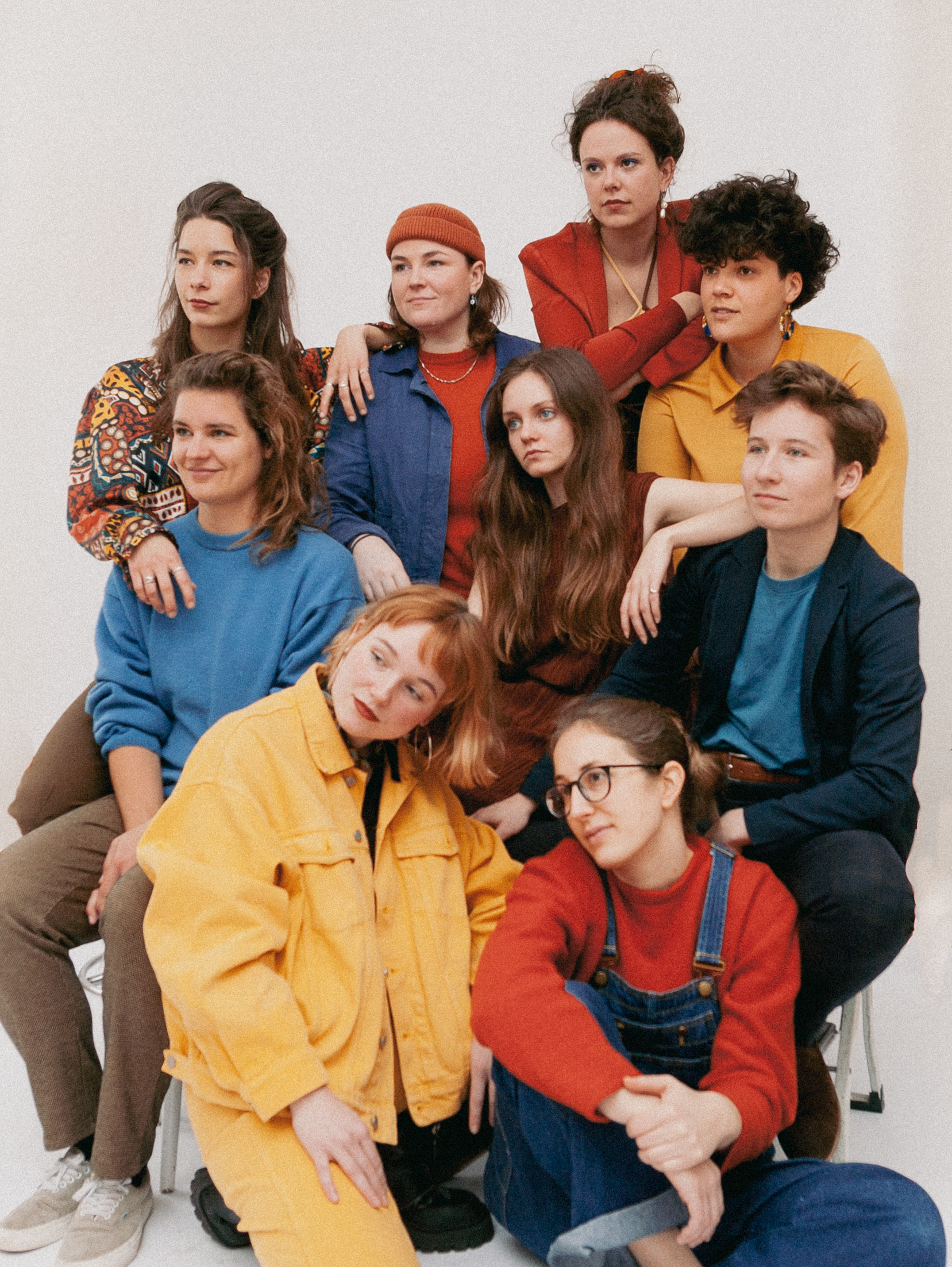 Dit is de persfoto van PARRA.DICE met de negen vrouwelijke/non-binaire bandleden. Ze zijn gekleed in het kleurpalette rood, blauw en geel.