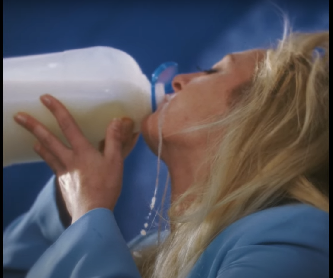 S10 drinkt hier van een pak melk en er druipt melk langs haar nek. Ze heeft een blauwe jas aan.