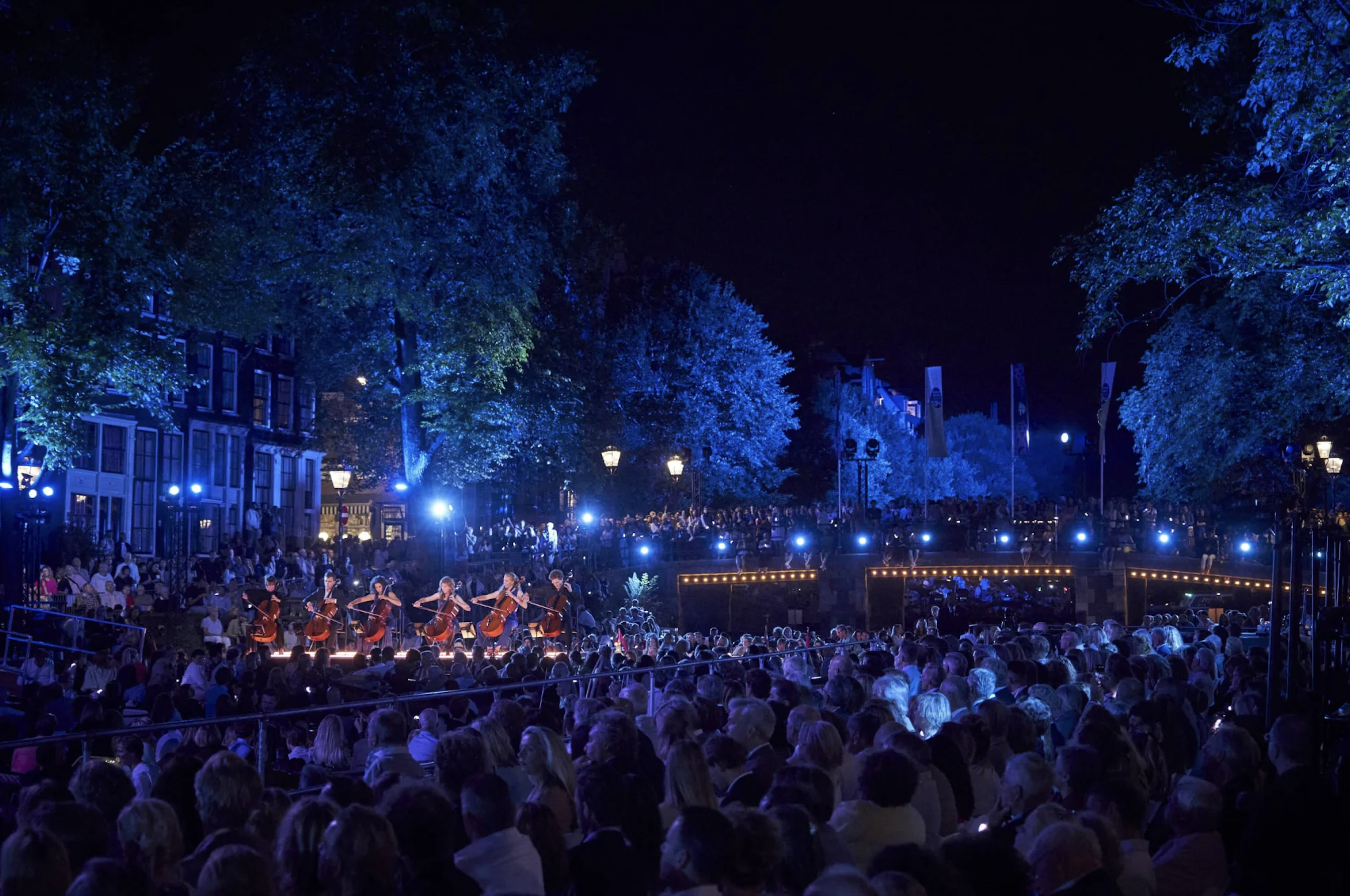 Een aantal violisten spelen op het Prinsengrachtconcert. Het is donker en de gracht is blauw verlicht.