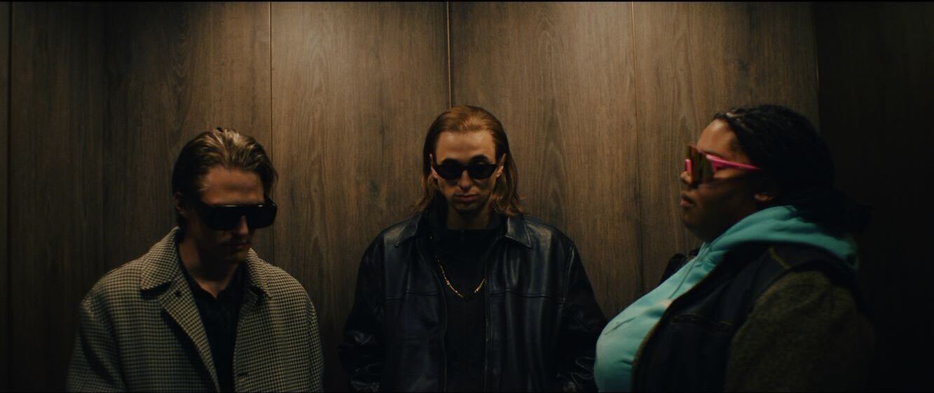De drie van de jeugd van tegenwoordig, maar dan acteurs, staan samen stoer kijkend in een lift