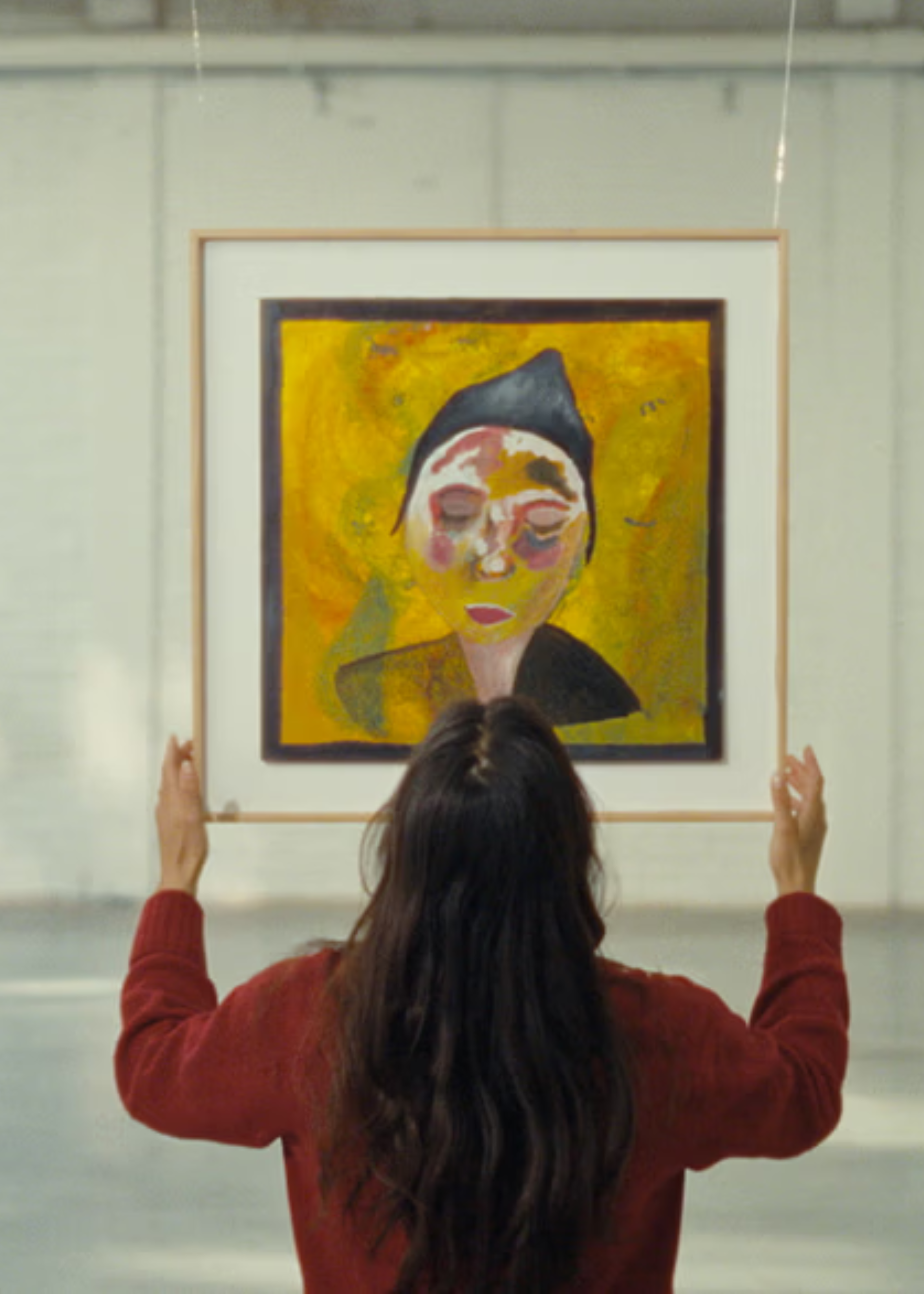 Vrouw kijkt naar een geel schilderij van een vrouw met een hoedje dat ze in haar handen heeft