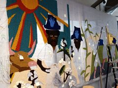 Deel van het wandkleed dat nog in constructie is. Je ziet een zon en twee mannen.