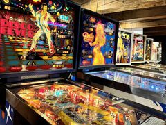 Twee lichtgevende flipperkasten naast elkaar. Links één in een discothema met een dansende man erop en rechts één met een Dolly Parton-thema.