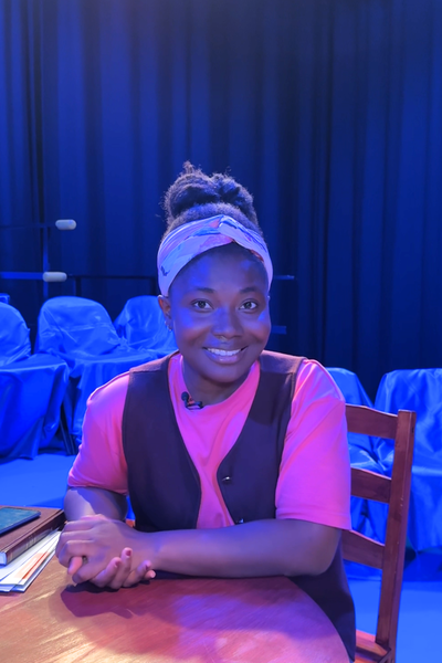 Op deze foto zien we Kimberley. Ze zit aan een tafel en kijkt vriendelijk lachend de camera in.