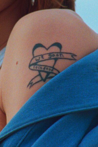 Blote schouder met tattoo. De tattoo is een hart met een lint eromheen, waarop staat 'We gaan toch dood'.