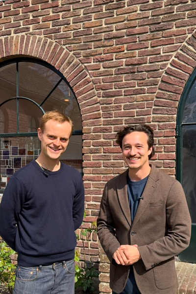 Foto van de twee hoofdrolspelers, Coen en Jurriaan. Ze staan voor een stenenmuur en kijken allebei vriendelijk de camera in.