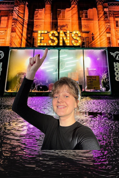 Foto van een plein in het donker, op een regenachtige avond. In het midden staat een gebouwtje met veel glas, met daarop lichtgevende letters ESNS. Daarvoor is een foto geplakt van Pieteke - de redacteur van dit artikel - die naar de letters wijst.