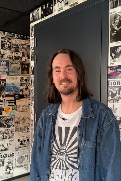 Portretfoto van artiestenbegeleider Mark. Mark kijkt vriendelijk de camera in en staat in een hal.