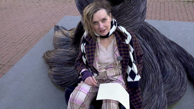 Anne Vegter zit bij standbeeld met dichtbundel