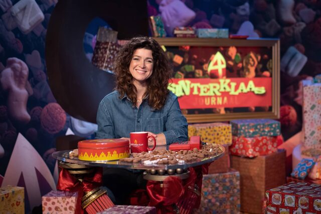 Merel Westrik zit aan haar presentatiedesk in het decor van Het Sinterklaasjournaal.