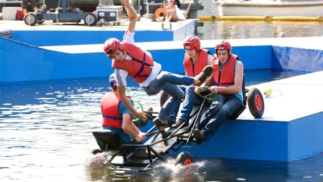Een kar valt met deelnemers in het water terwijl de bel wordt geluid