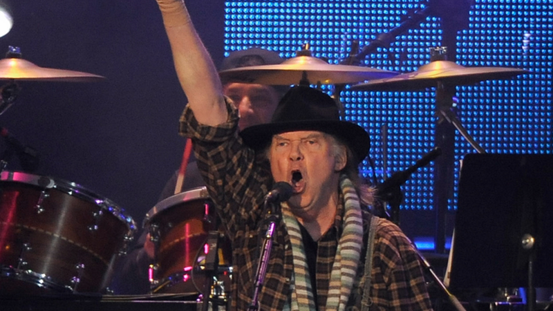 Neil Young treedt op en steekt zijn vuist in de lucht tijdens het zingen.