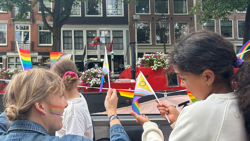 Een meisje en een mevrouw van Theater De Krakeling zwaaien met vlaggetjes naar de voorbijgangers vanaf de boot in Amsterdam.