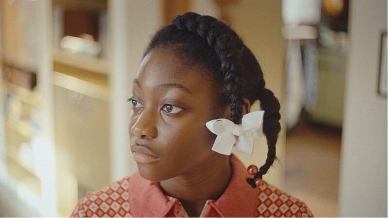 Meisje met witte bloem in haar vlecht kijkt naar iets dat buiten de camera is