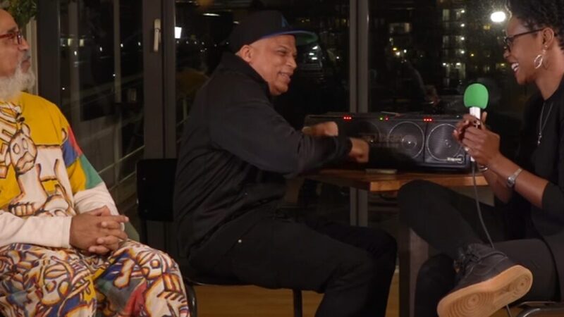 Drie mensen zitten lachend rond een tafel met een dj-set aan