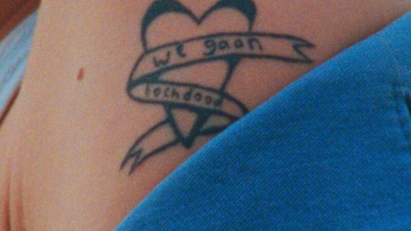 Blote schouder met tattoo. De tattoo is een hart met een lint eromheen, waarop staat 'We gaan toch dood'.