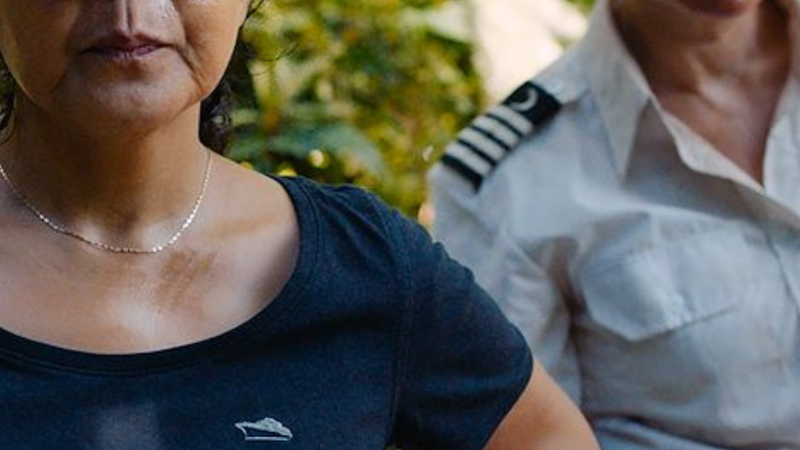 Er staan twee vrouwen op het beeld. De linker vrouw staat met haar handen in haar zij en heeft een zwart T-shirt aan en een zwarte pet op. De rechtervrouw heeft kort geblondeerd haar en heeft een kapiteinkostuum aan.