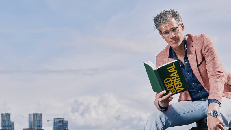 Erik Dijkstra zit op een steen met een boek in zijn hand kijkend naar de camera