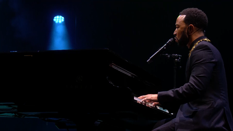 Zanger John Legend zit in een zwart pak achter zijn vleugel te zingen