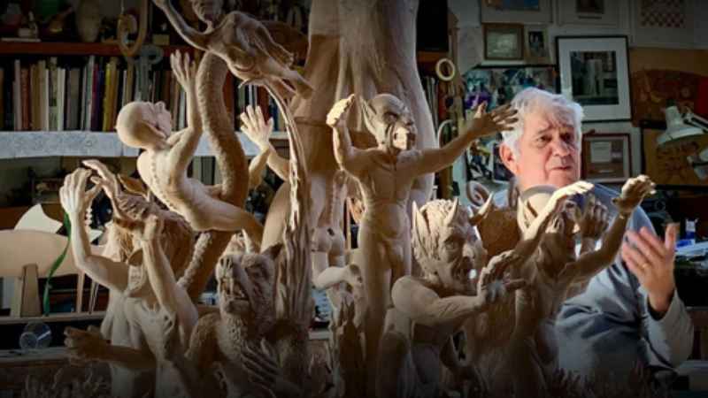 Jimmy Grashow die iets vertelt met handgebaren, achter zijn kunstwerk.