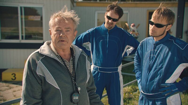 Drie witte mannen spelen hun rol in de serie Schwalbe. Links staat de wat oudere trainer en rechts staan de twee stuurlopers in blauwe pakken met zwarte zonnebrillen.