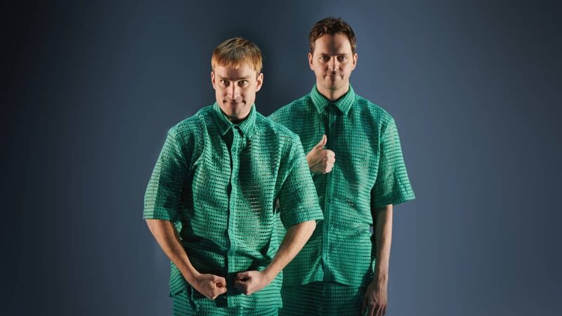 Twee witte jongens in een groen pak kijken verdwaald naar de camera tijdens hun theatervoorstelling