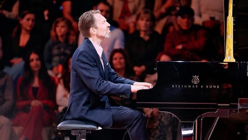 Noorse pianist zit achter een zwarte vleugel op een podium