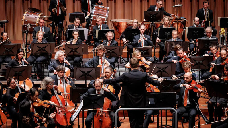 Podium vol met muzikanten uit een symfonieorkest met een dirigent ervoor