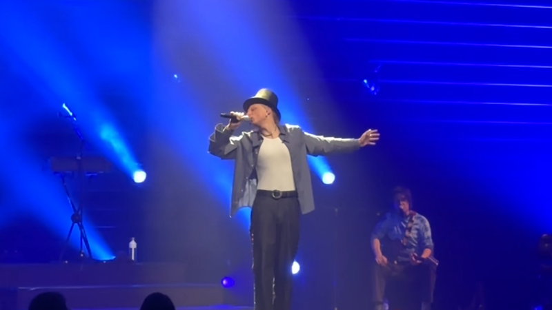 Foto van Scott tijdens de theatershow. Hij staat op een groot podium met podiumlampen en hij heeft een hoge hoed op.