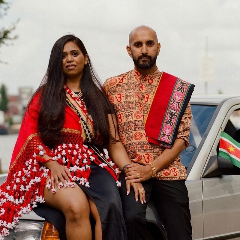 Een man en een vrouw gekleed in traditionele kleding leunen tegen een grijze mercedes.