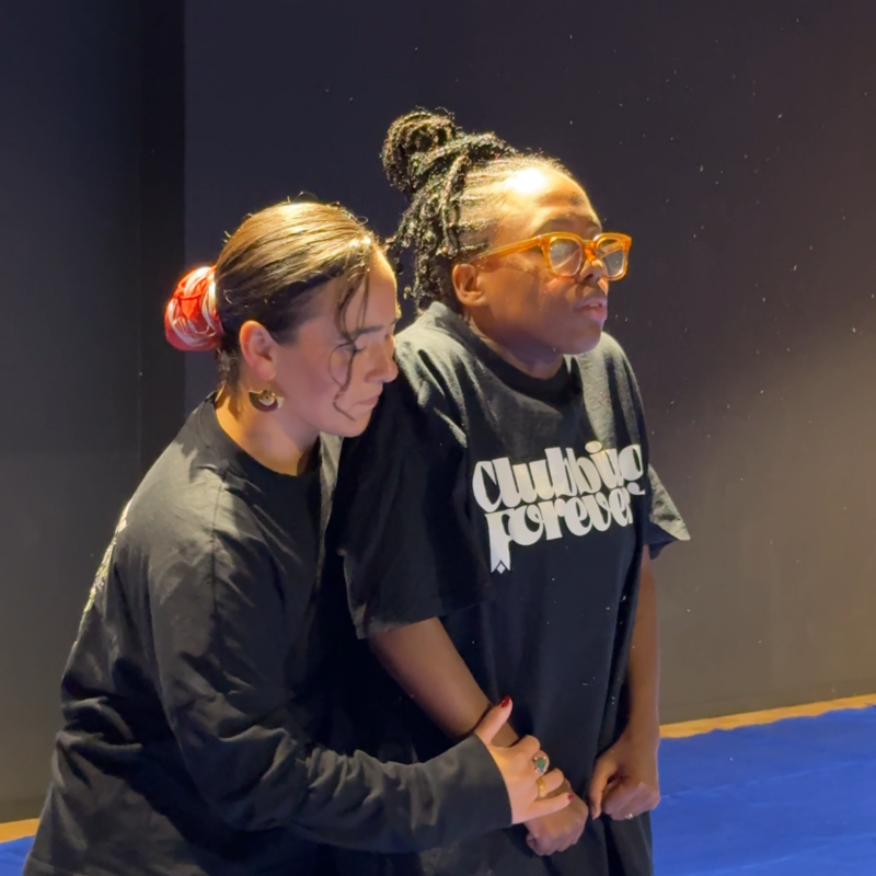 Een beeld uit de voorstelling DIEP. Meis en Jasmin staan samen op het toneel en Meis houdt Jasmin liefdevol vast. Je ziet duidelijk dat het twee vriendinnen zijn die elkaar helpen.