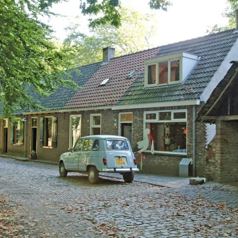 Straat met Tilburgse arbeidershuisjes. Voor een van de woningen staat een auto en op straat liggen herfstbladeren.