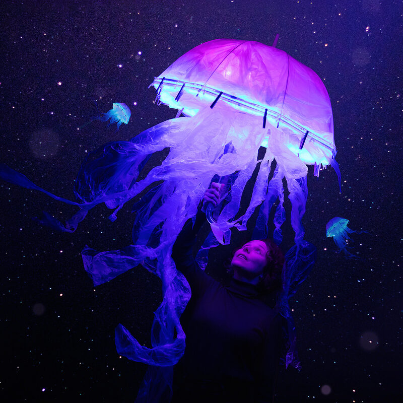 Foto van een lichtgevende kwal (een pop) in de voorstelling DIEP. Hij is paars/blauw voor een donkere achtergrond met kleine lampjes.