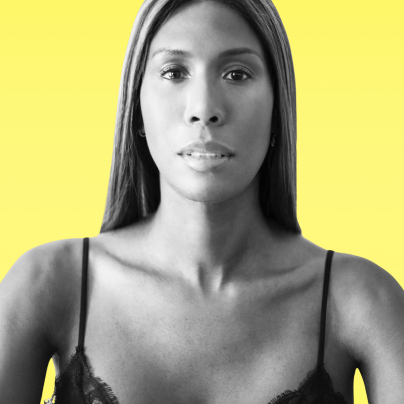 Een foto van Honey Dijon, in ene kanten top, voor een gele achtergrond.