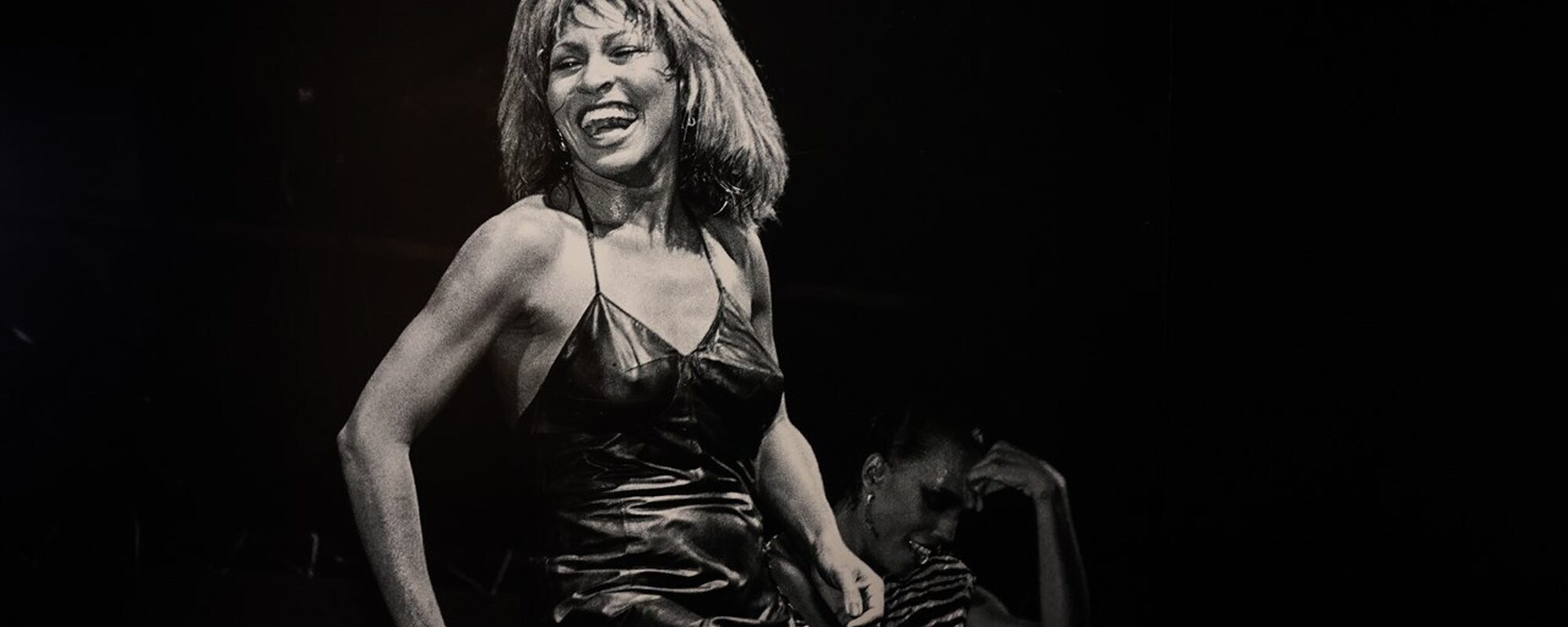 Zwart wit foto van een dansende en lachende Tina Turner