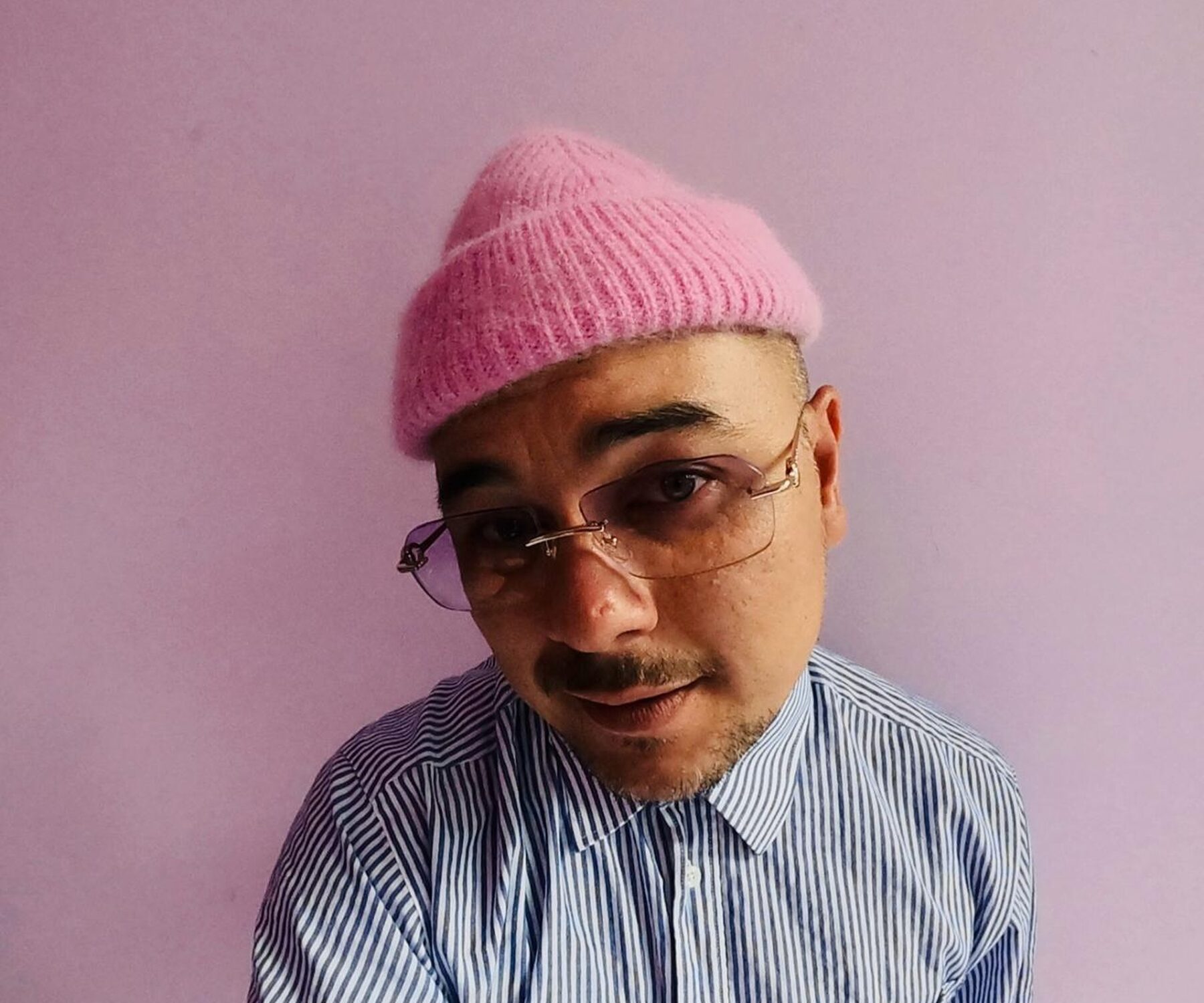 Een foto van (radio) DJ Justin Verkijk. Hij staat voor een roze achtergrond en heeft een roze muts op. Hij houdt zijn hoofd een beetje scheef en kijkt de camera in.