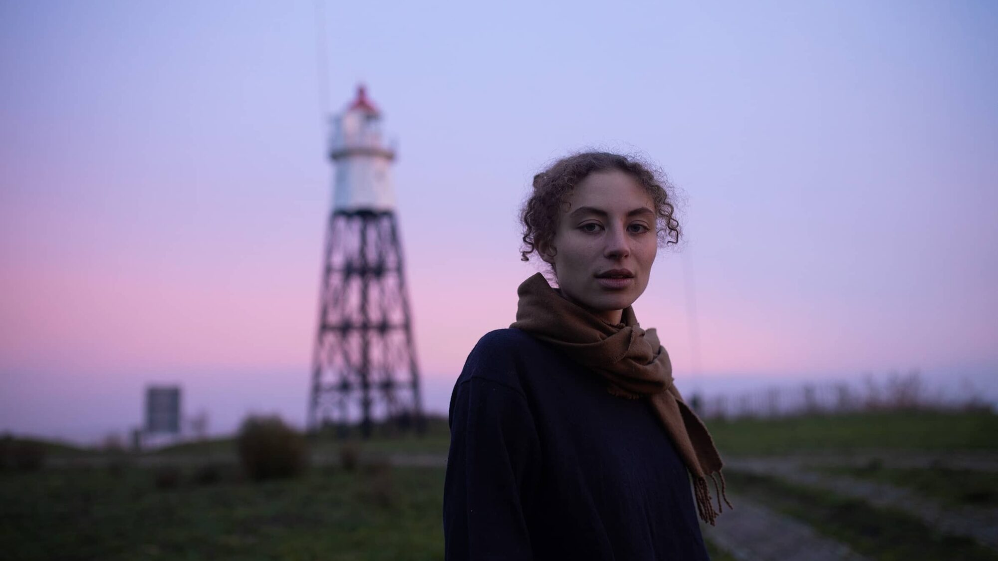 Sarah Neutkens staat bij een spoor tegen een paarse lucht aan en kijkt de camera in.