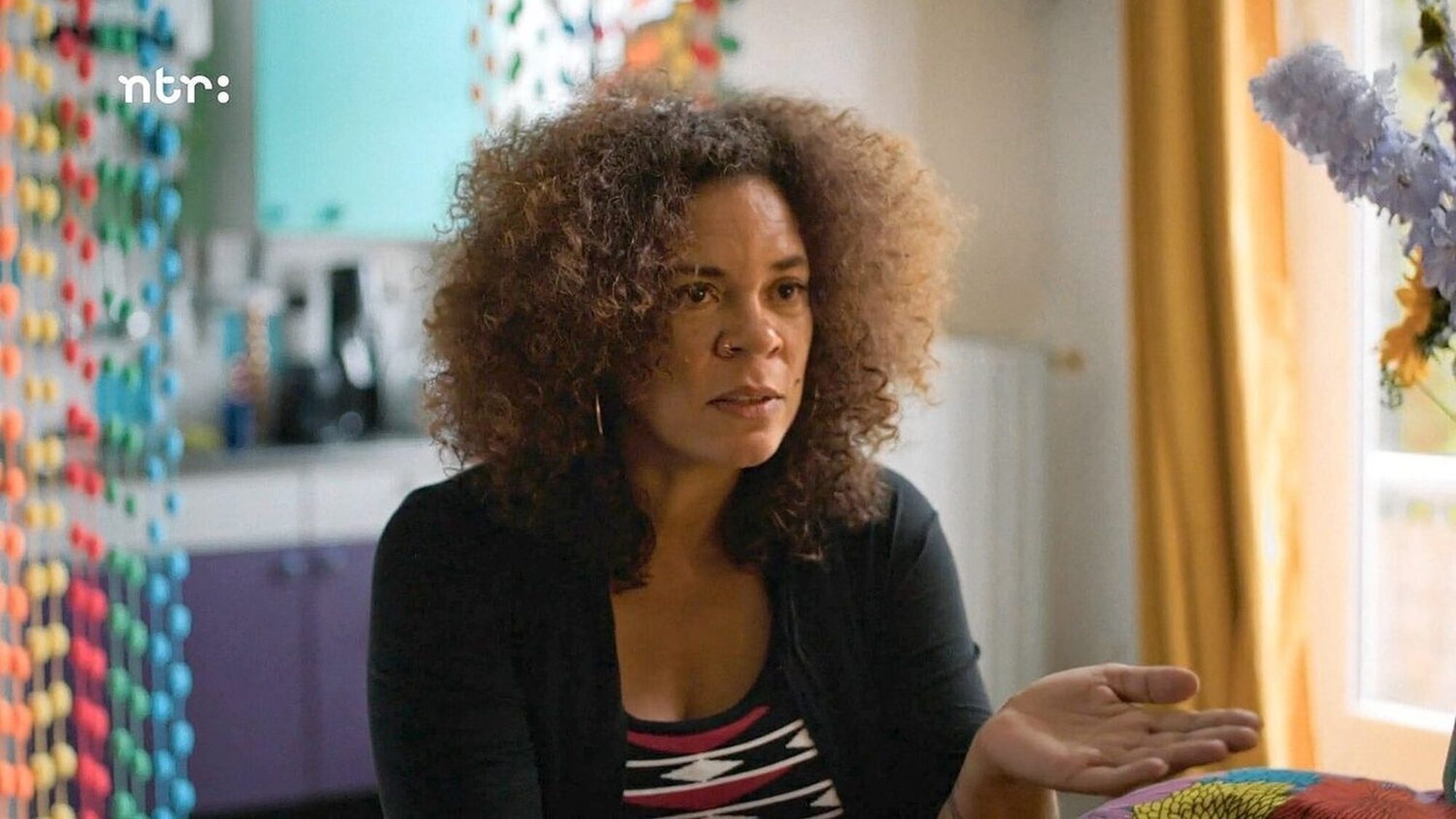 een stil uit de documentaire over babs gons. We zien haar hier praten naar iemand naast de camera, in een kleurrijke omgeving.