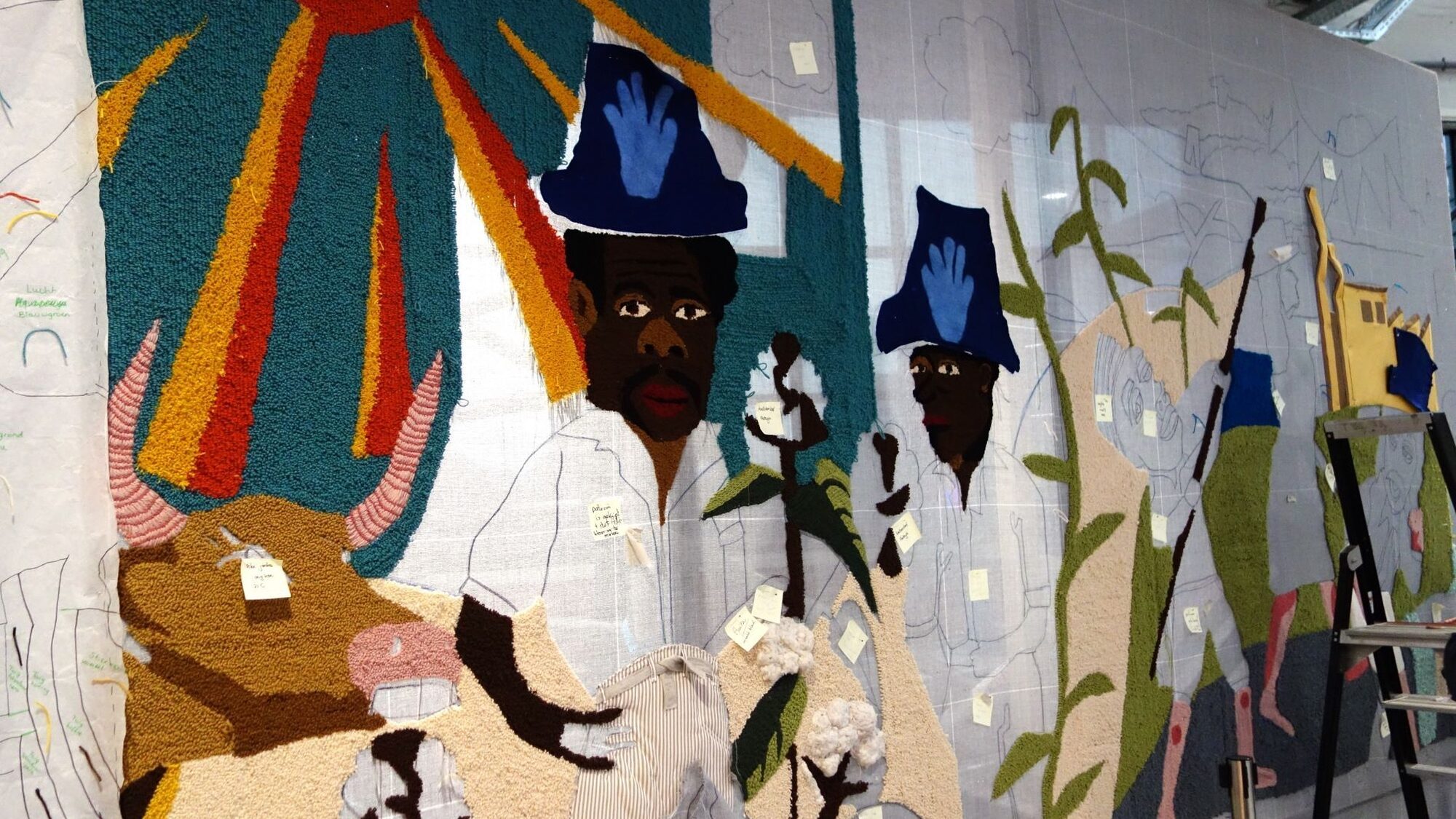 Deel van het wandkleed dat nog in constructie is. Je ziet een zon en twee mannen.